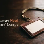 Worn leather owner's badge holder on a dark oak desk beside the headline Do Owners Need Workers' Comp
